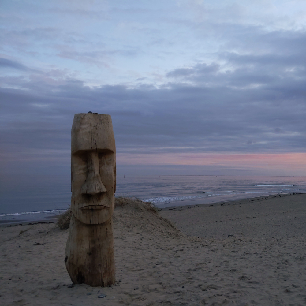 A empty beach in the late evening sunset. There is a wooden totem carved into the shape of a human face.